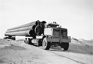 Ancienne photo d’un camion Kenworth transportant de gros tuyaux sur un chantier de construction